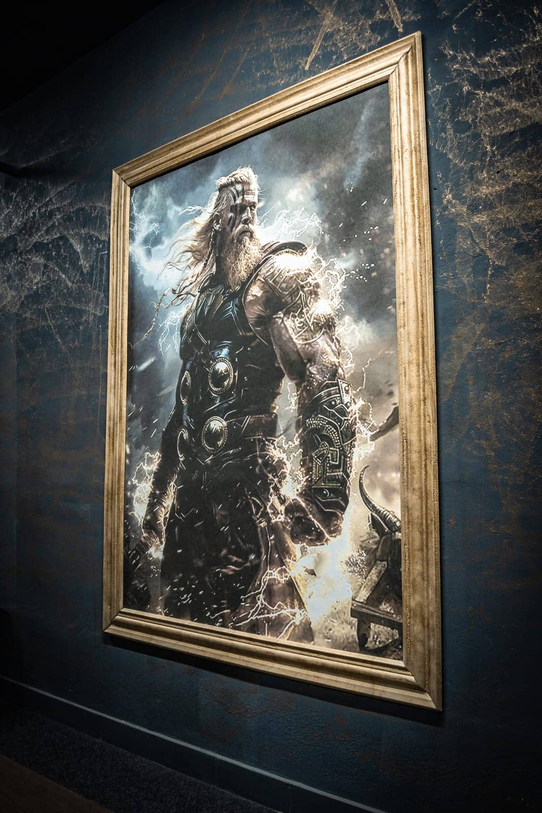 Fotoobraz severského bojovníka s bleskami v zlatom ráme na tmavomodrej stene posilňovne Asgard Gym