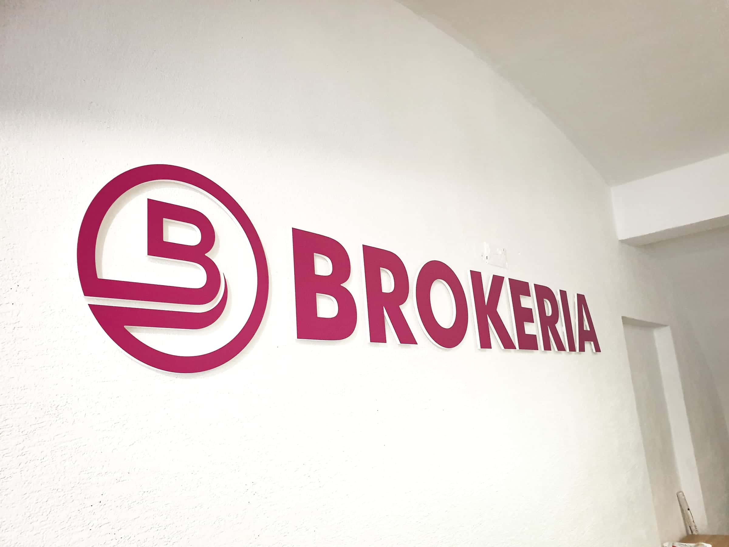 Priestorové purpurové 3D logo BROKERIA na bielej stene