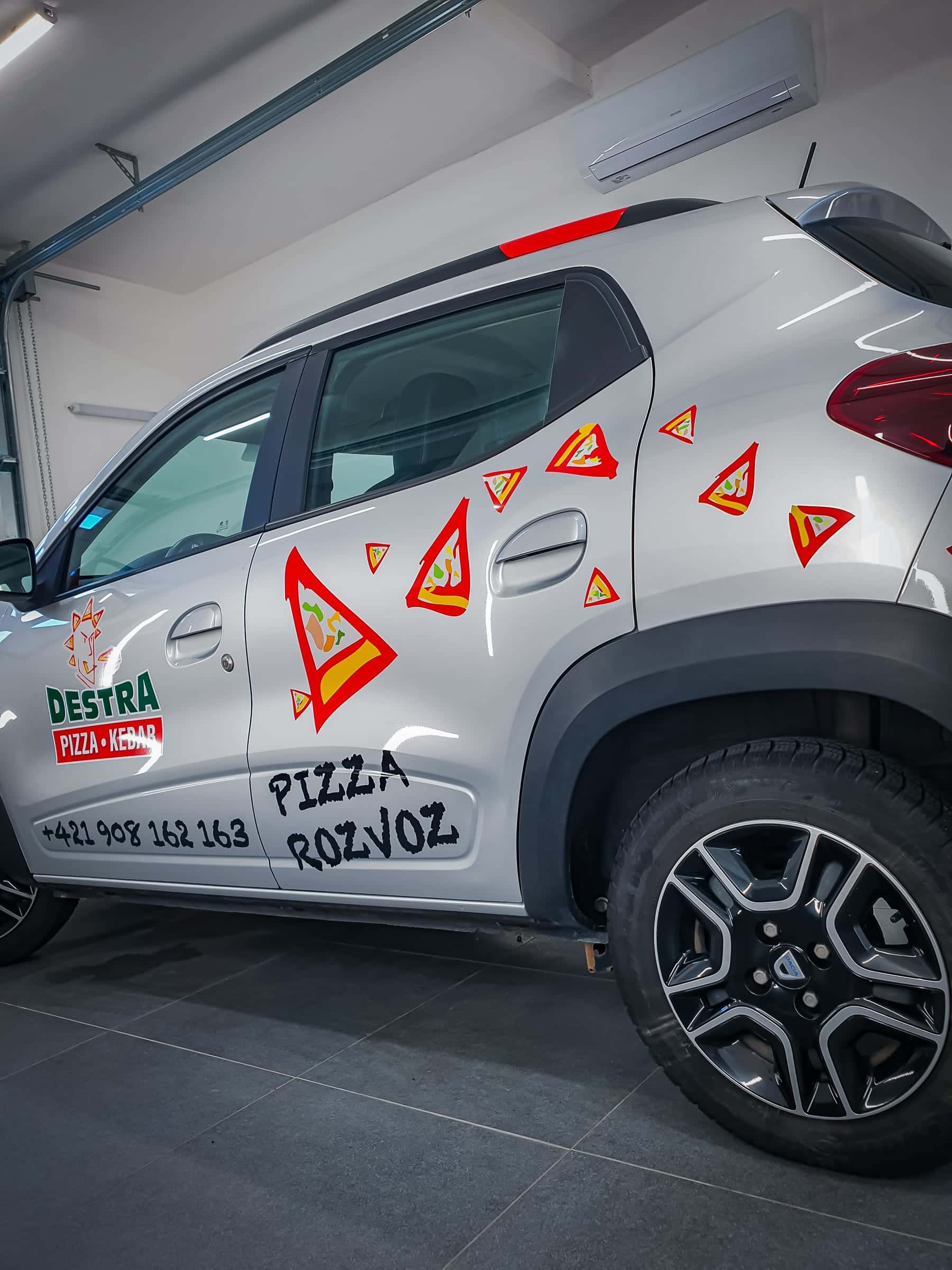 Bok Dacie Spring s polepom kúskov pizze a nápisom Pizza rozvoz