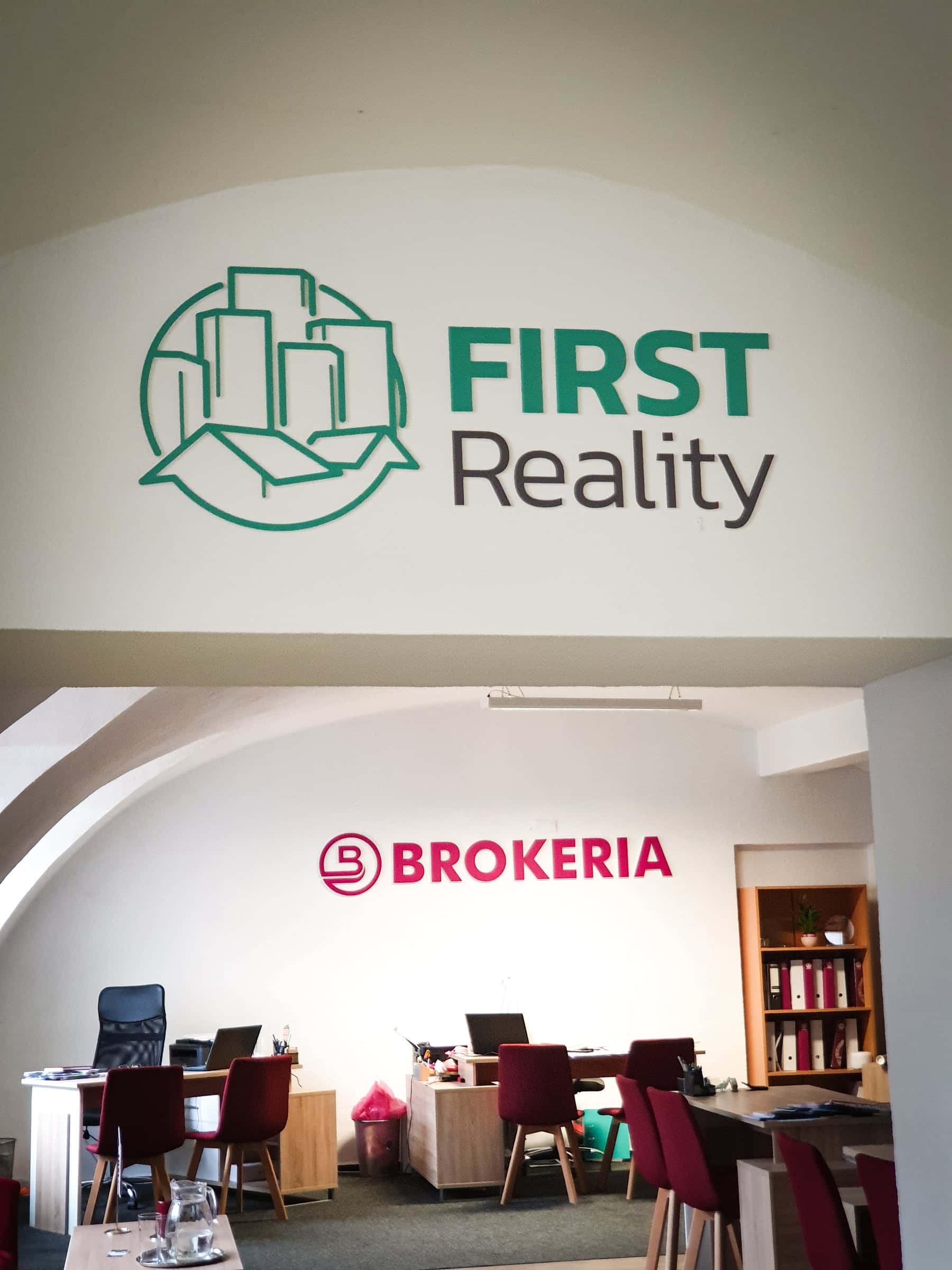 Priestorové 3D logo First Reality na klenutej stene, pod ním kancelária s logom BROKERIA