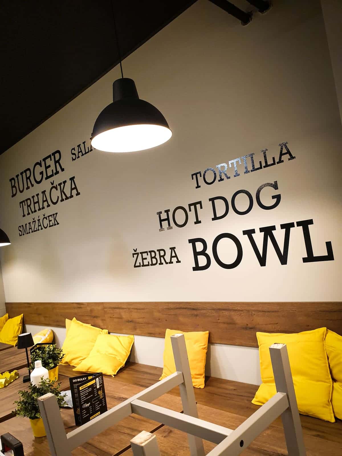 Rezané nápisy jedál – burger, hot dog, bowl – na stene bistra