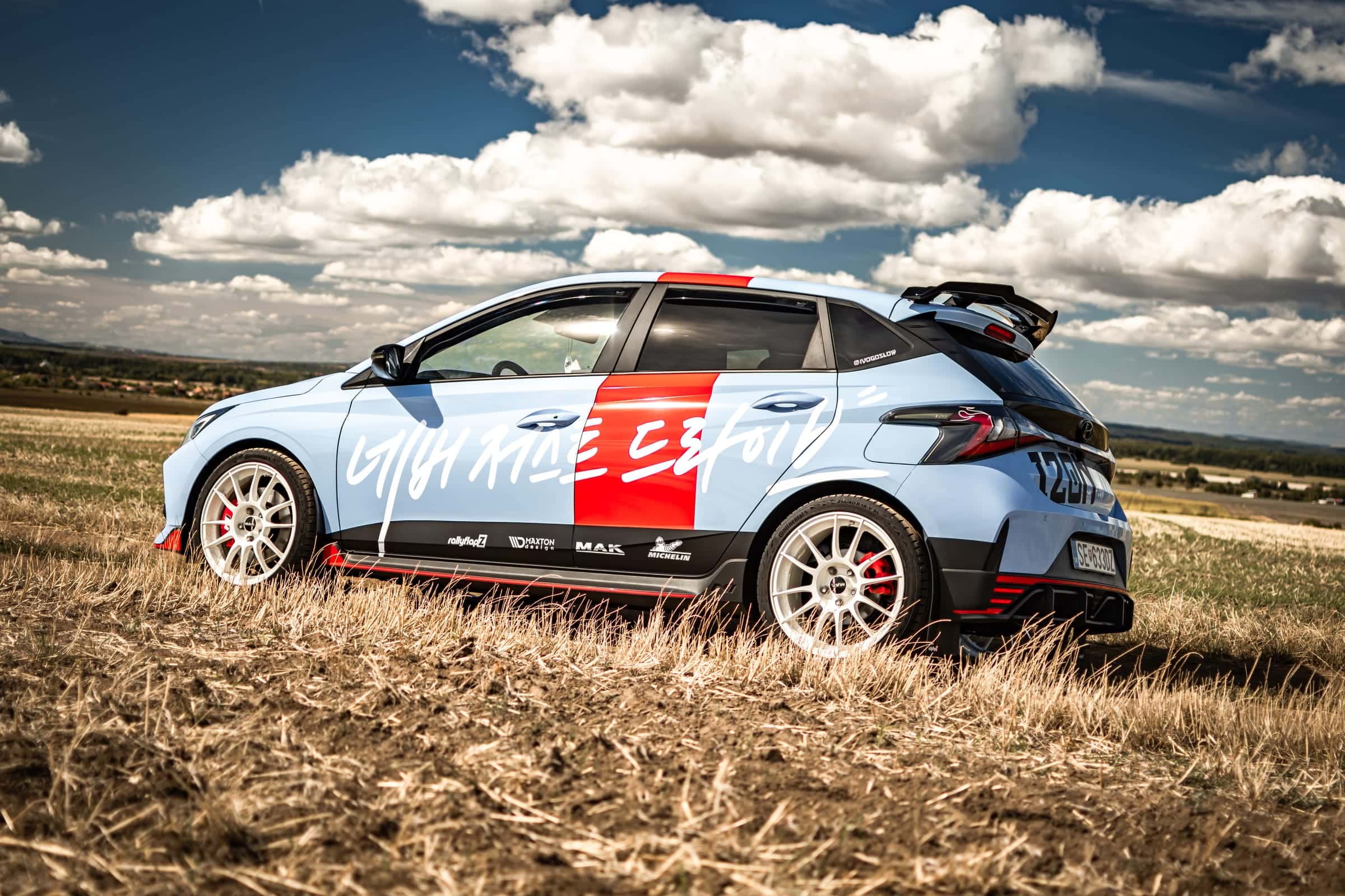 Svetlomodrý Hyundai i20 N s polepom Project LIL-N zozadu zboku v poli pod dramatickou oblohou