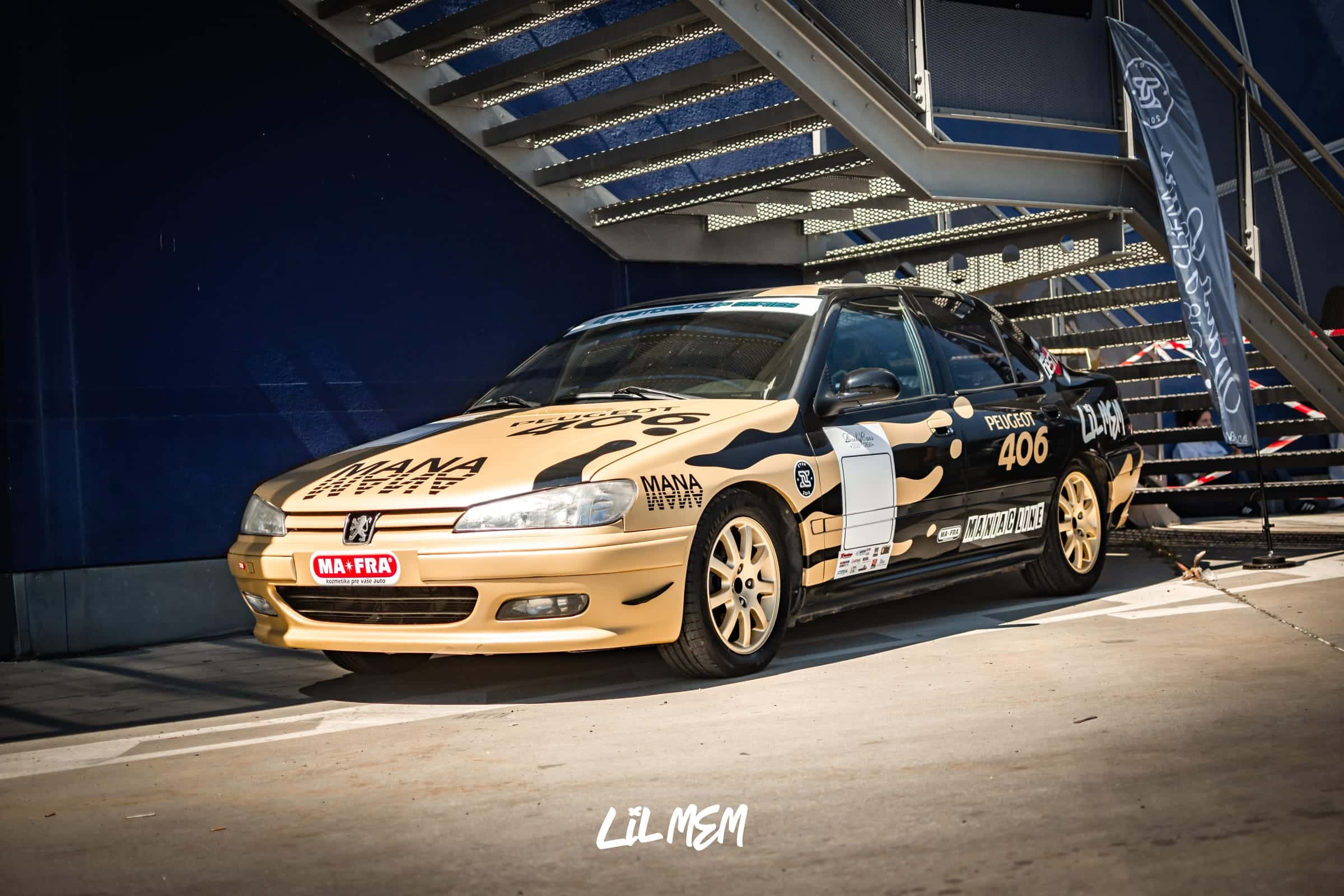 Okruhový Peugeot 406 tímu Daily Cars Crew s béžovo-čiernym závodným polepom a nápisom Peugeot 406 na dverách v depe pod schodiskom
