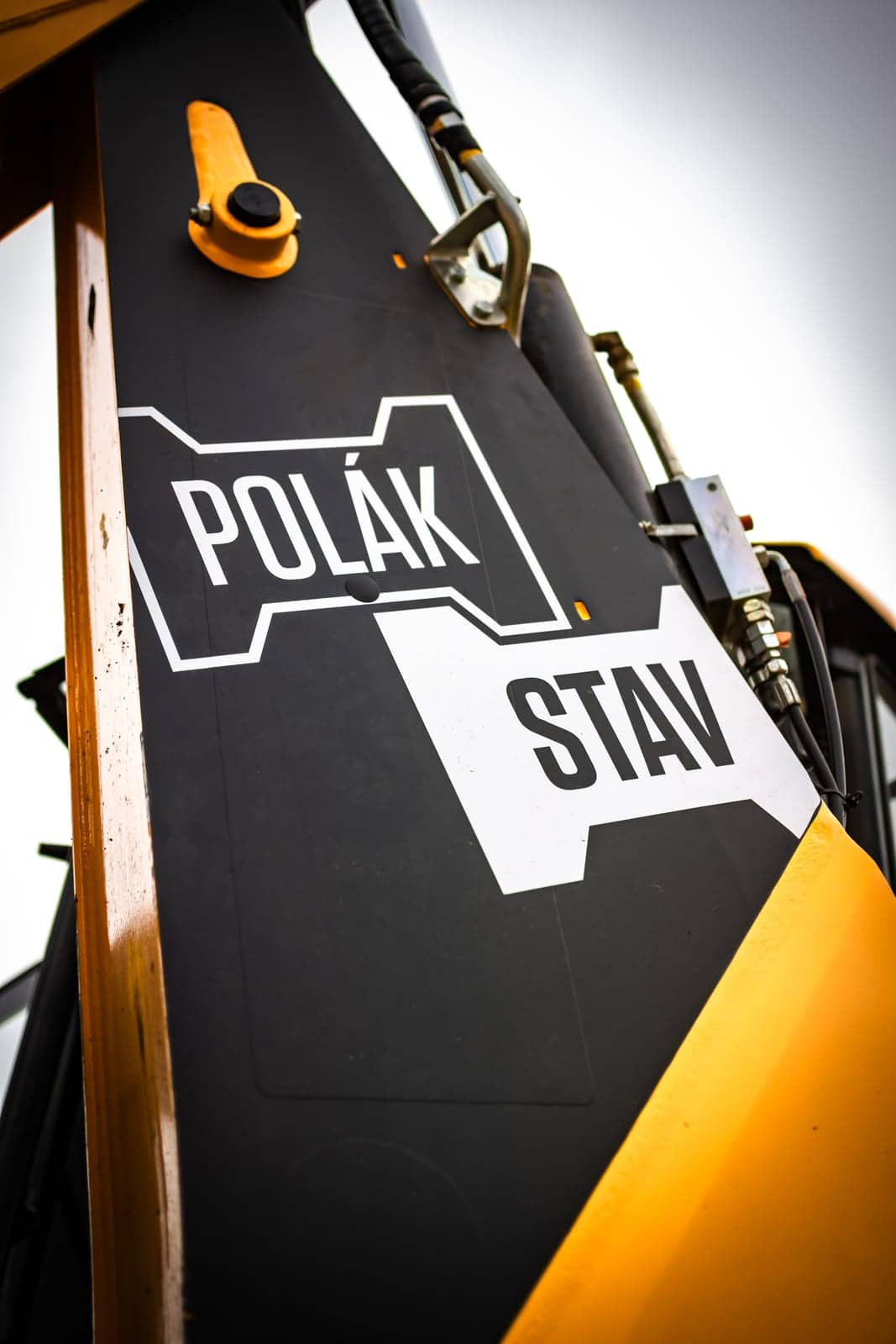 Logo POLÁKSTAV na čiernom ramene žltého bagra, záber zdola proti oblohe