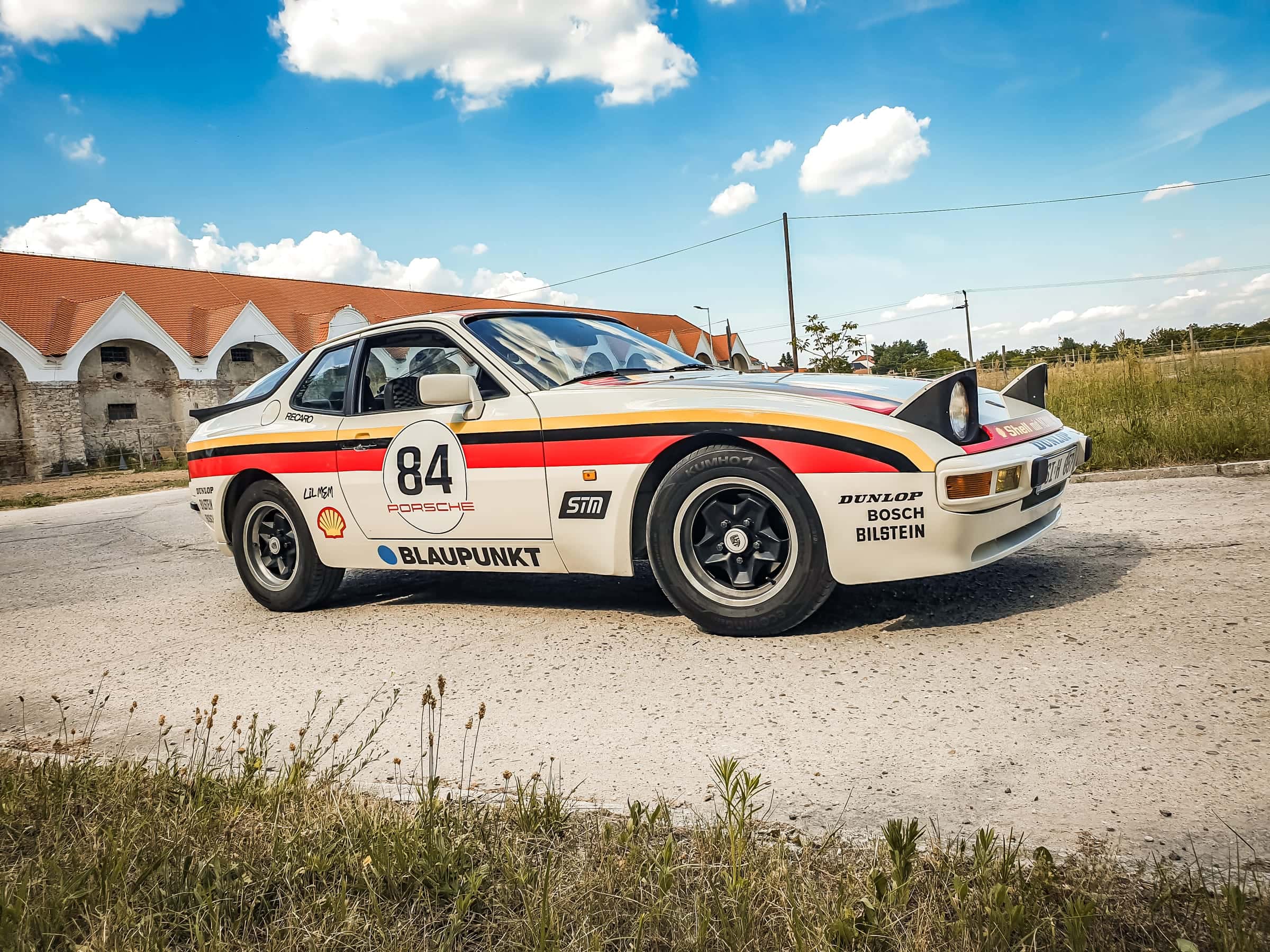 Biele Porsche 944 s retro pretekárskym polepom v nemeckých farbách, číslom 84 a logami sponzorov pri statku