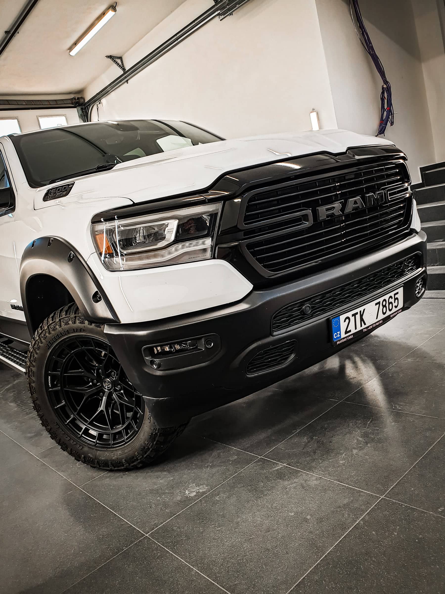 Biely pick-up RAM 1500 s čiernou maskou a nápisom RAM po dechróme v dielni