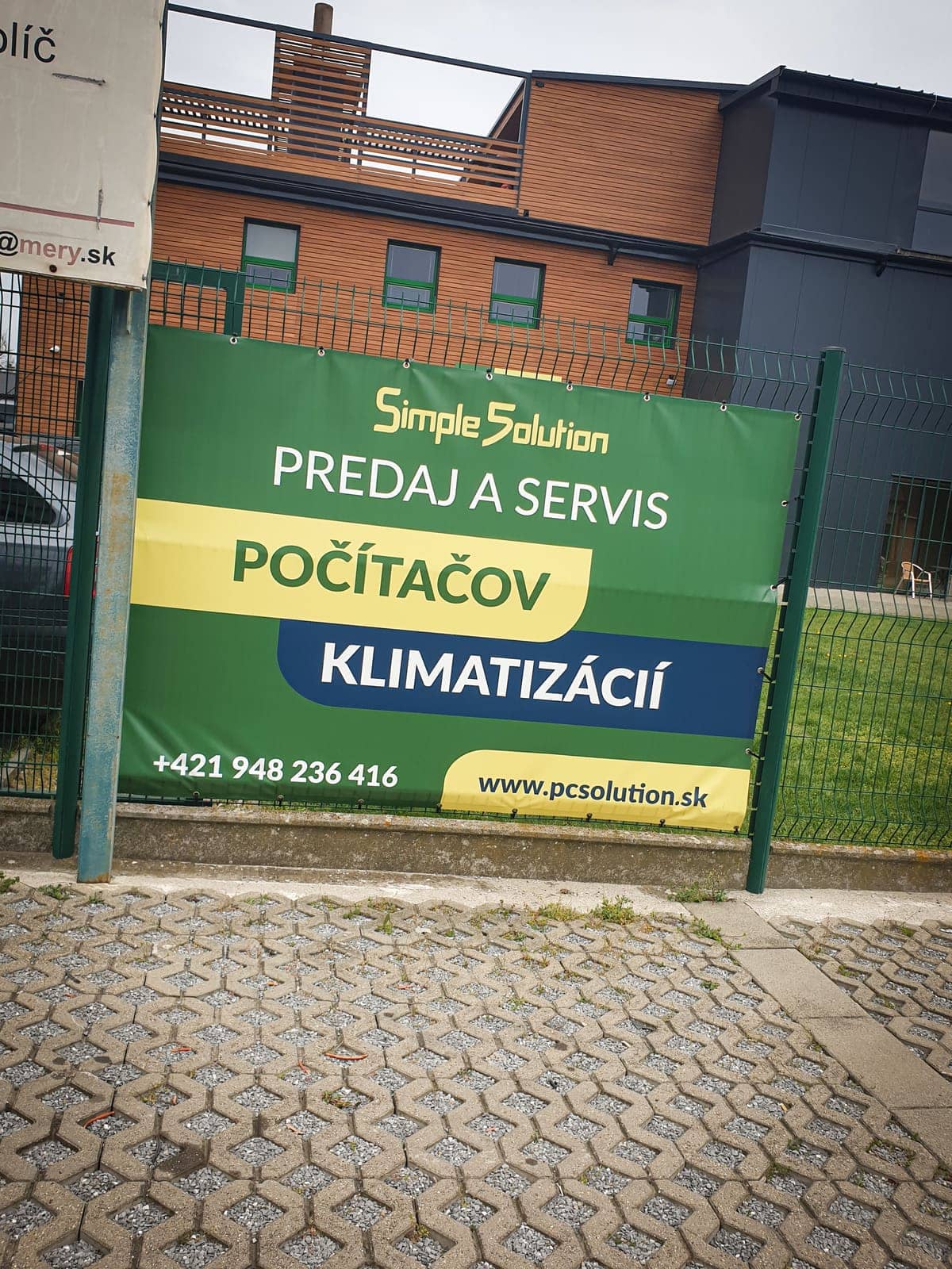 Banner Simple Solution – predaj a servis počítačov a klimatizácií – na plote pred budovou
