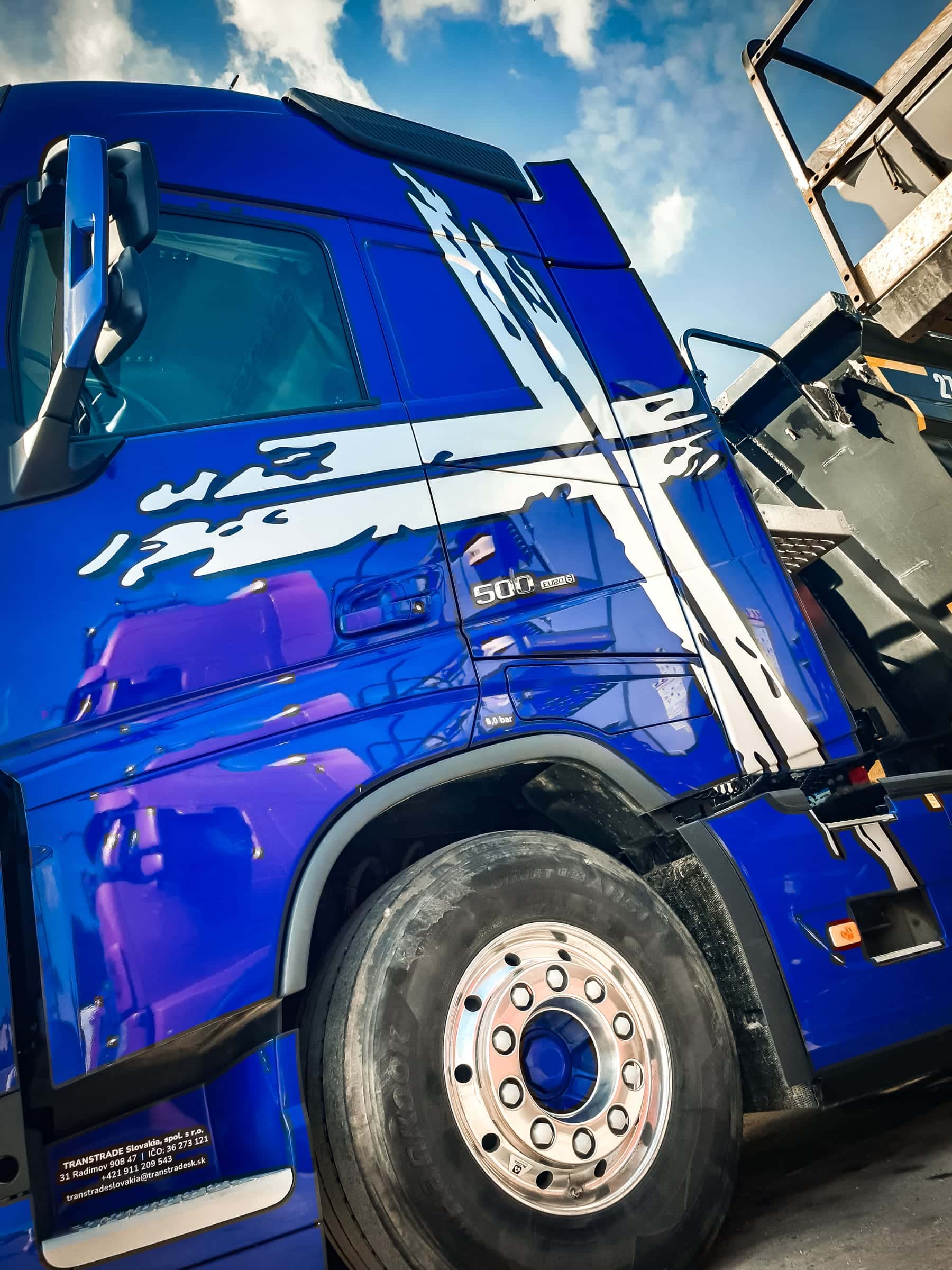 Modrý ťahač Volvo FH 500 s bielym grafickým polepom kríža a nápisom Transtrade na dverách